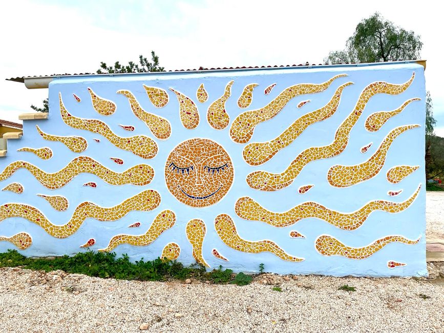 The tile mosaic of a large sun decorates a concrete wall.