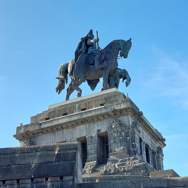 Das Kaiser-Wilhelm-Denkmal Kurz nach dem Tod von Kaiser Wilhelm I., entstand die Idee, dem Kaiser, der nach drei Kriegen die vollendete Einigung Deutschlands herbeigeführt hatte, ein Denkmal zu setzen. Drei Jahre später, 1891, wählte Kaiser Wilhelm II., der Enkel des Verstorbenen, das Deutsche Eck in Koblenz als geeigneten Ort. Um Platz für das Denkmal zu schaffen, wurde ein Nothafen zugeschüttet, der sich zu dieser Zeit an der Moselmündung befand. Das Deutsche Eck in seiner heutigen Form entstand. Am 31.08.1897 wurde das aus Kupfer angefertigte Denkmal von Kaiser Wilhelm I. in Anwesenheit von Kaiser Wilhelm II. feierlich eingeweiht.