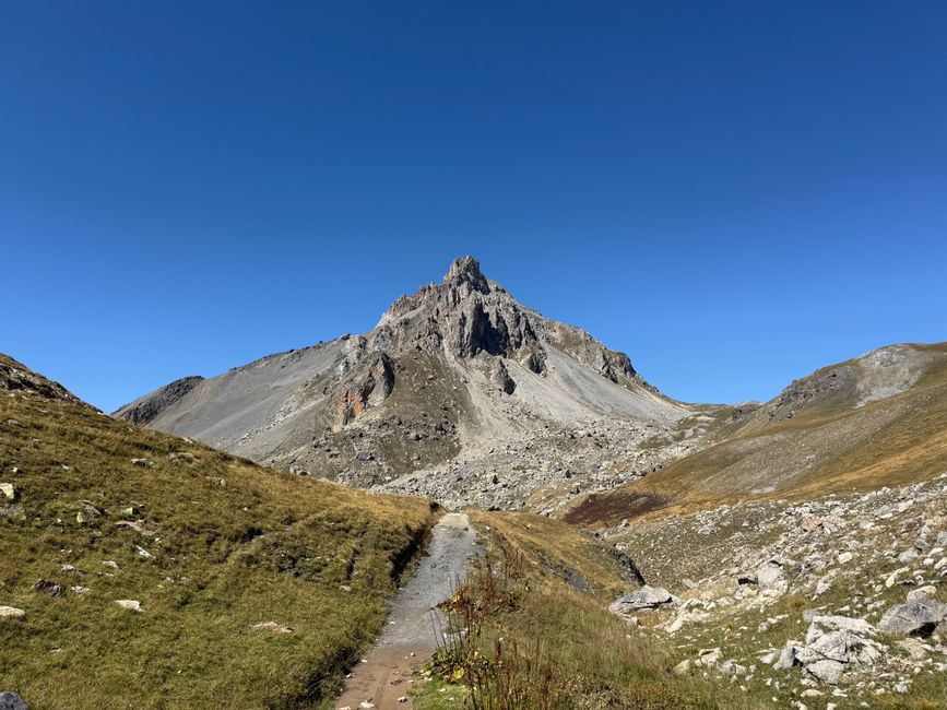 L'unico commento sotto questa relazione era che era pericoloso per la vita e si sconsigliava vivamente di farlo. Quindi il mio interesse è stato catturato. Tuttavia, non avrei provato a farlo come traversata ma avrei preso la via di discesa per poter tornare indietro in tempo se necessario.</p><p style='color:rgb(0, 0, 0)'>Senza zaini, riuscivo a sollevare bene la bici con il mio sistema di trasporto, e quindi si partì. Secondo la descrizione c'erano passaggi esposti dove era meglio spingere di tanto in tanto, e in fondo dovrebbe essere S2-S3. La mia impressione era diversa. Sebbene ci fossero passaggi percorribili nella parte bassa. Questi erano però costantemente interrotti da smottamenti più piccoli sopra i quali dovevo faticare per sollevare la bici. Era già chiaro durante la salita che durante la discesa non ci sarebbero stati sentimenti di flow. Non andò nemmeno meglio. Al contrario, a 2500 metri la strada si impenna ulteriormente e incrocierebbe di nuovo i smottamenti dopo una curva. Ho rinunciato, con la bici non aveva più senso. Ma a piedi volevo comunque raggiungere la cima. E quello fu un bel arrampicarsi di difficoltà T3, dove anche le mani erano necessarie, e che era anche un po' aereo. Con le rocce ripide e le torri simili, sembrava di essere nelle Dolomiti. E dato che eravamo in un'area di confine con la Francia, non mi sorprendeva trovare un piccolo bunker di nuovo sulla cima. In ogni caso, come poterono costruirlo all'epoca senza un elicottero è un mistero. E come possa essere pubblicato come tour in mountain bike non mi è chiaro. Certo, se durante il tempo libero si partecipa attivamente alla Red Bull Rampage, ci si diverte sicuramente in qualche punto. Per tutti gli altri sarebbe una prova di coraggio piuttosto priva di senso portare la bici su e giù. Tornato alla bici, per la breve discesa ho scelto la diretta sulla pietraia. È andata abbastanza bene in un certo modo.</p><p style='color:rgb(0, 0, 0)'>Il campeggio era poi da sogno. A sinistra di me il potente Monte Scaletta, con un piccolo bubbone grazie al bunker di vetta. Davanti a me si increspa il Lago di Roburent, una piscina naturale infinita in alto sopra la Valle Stura. A causa dell'emozione per la scalata pomeridiana della cima, avevo già dimenticato che in realtà doveva essere freddo. Ma il sole ha fatto un ottimo lavoro nel pomeriggio. Poco prima che volesse scomparire di nuovo, ho goduto degli ultimi raggi caldi. Poi è diventato gelido. Questa notte dovevo davvero usare tutto l'arsenale di vestiti che avevo con me. Anche i pantaloni lunghi vennero messi in uso. Beh, con il mio sacco a pelo estivo, la temperatura di comfort era solo di +5 gradi. E quella notte le temperature sono scese per la prima volta così in basso che si è formata la brina sulla mia tenda esterna. Brrr. Ma la luna piena splendente, che mi guardava con indifferenza mentre tremavo e si rifletteva nel lago, era semplicemente spettacolare.</p>