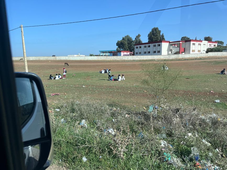 Straßenszenen #3: Schulkinder sitzen vor der Schule auf der (vermüllten) Wiese - scheint nicht zu stören