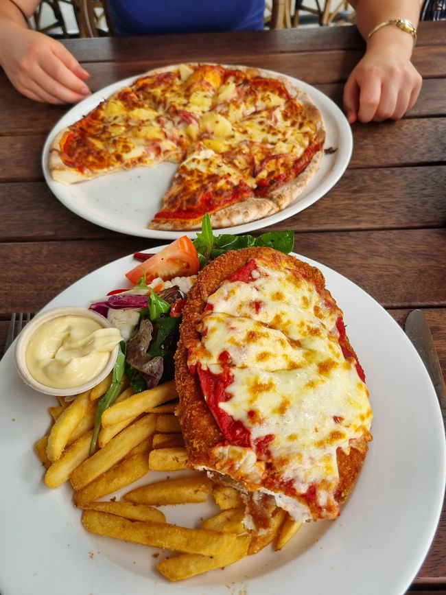 unten Chicken Parmigiani oder Chicken Parmy, ein australisches Gericht mit paniertem Huhn, Schinken, Tomatensauce und Käse