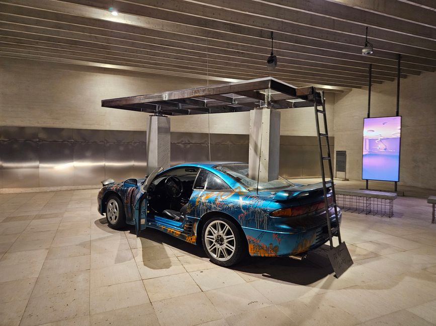 Nordischer Pavillon (Finnland, Norwegen, Schweden): Ein zerstörtes Auto als Symbol für die fossile Industrie und den Wandel von Körper, Architektur und Umwelt.