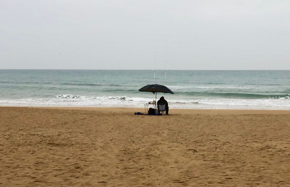 This fisherman sits alone and abandoned on the beach in the pouring rain and hopes for his luck.