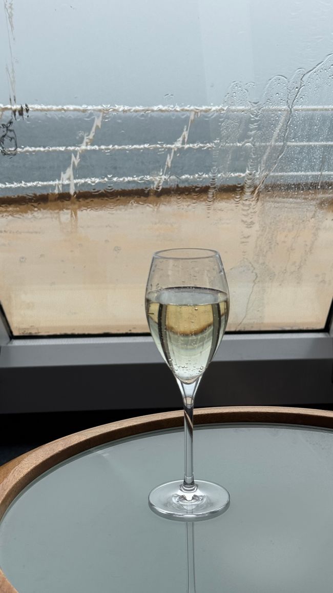 Bugfenster mit Regen außen und Prosecco innen
