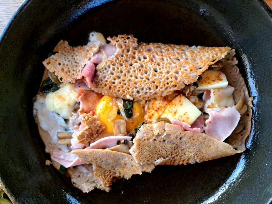 Frische handgemachte, goldbraun gebackene Galette aus heimischem Bioweizenmehl mit einer pikanten Füllung aus oignon rouge, jambon de porc, poireau de crau, champignon de paris und fromage Saint-Nectaire mit einem Bio-Ei-Topping von fröhlich gackernden Hühnern der Nachbarschaft