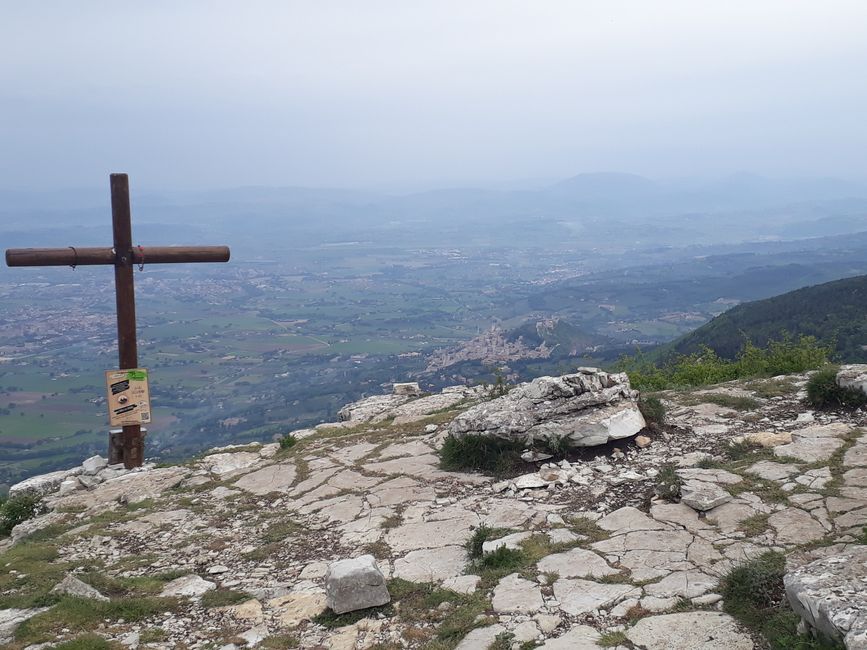 Das Gipfelkreuz an einer sehr steilen Hangkante,  unten im Tal: Assisi